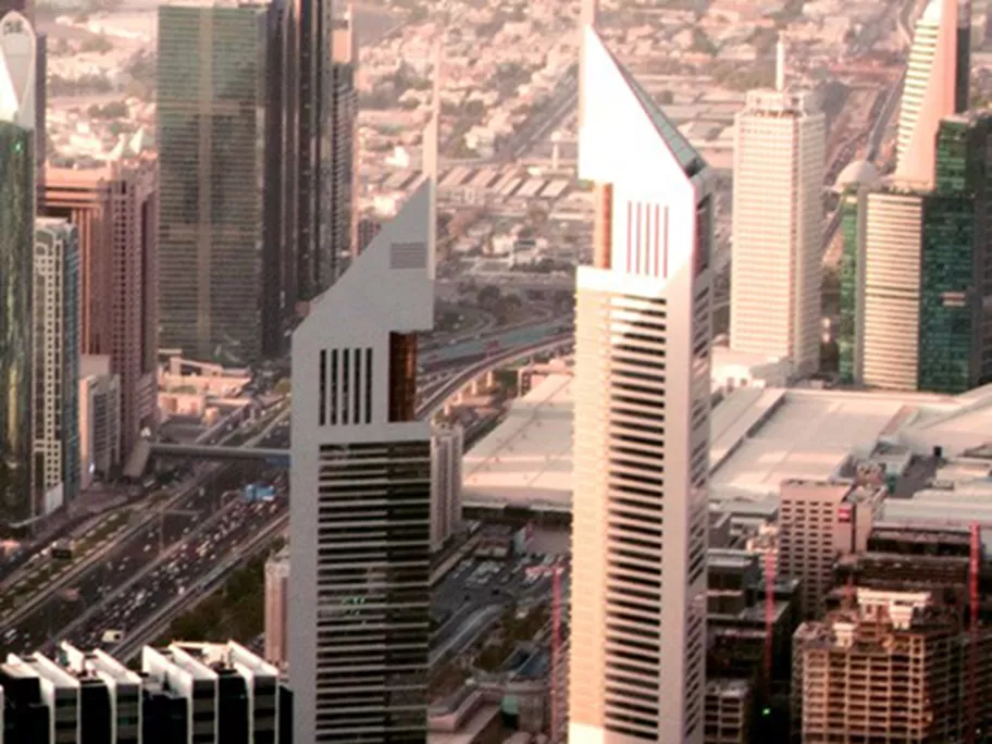 A close-up aerial view of the Emirates Towers in Dubai, rising prominently along Sheikh Zayed Road