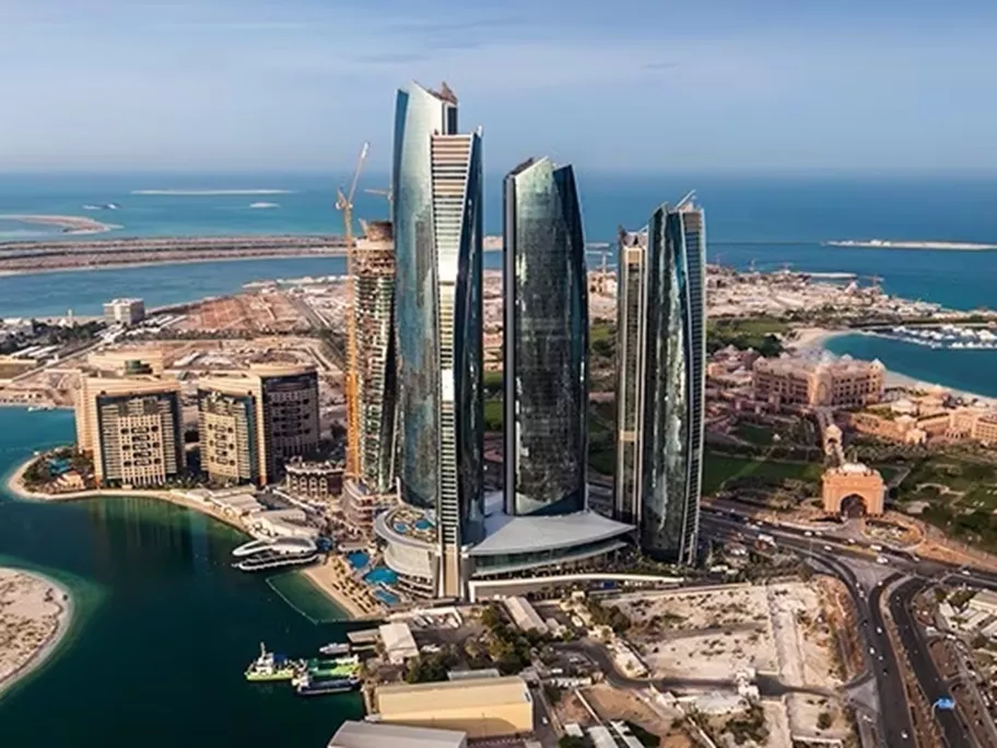 The striking Etihad Towers complex in Abu Dhabi, with its five futuristic high-rises overlooking the turquoise waters of the Arabian Gulf, surrounded by upscale developments and the nearby Emirates Palace.
