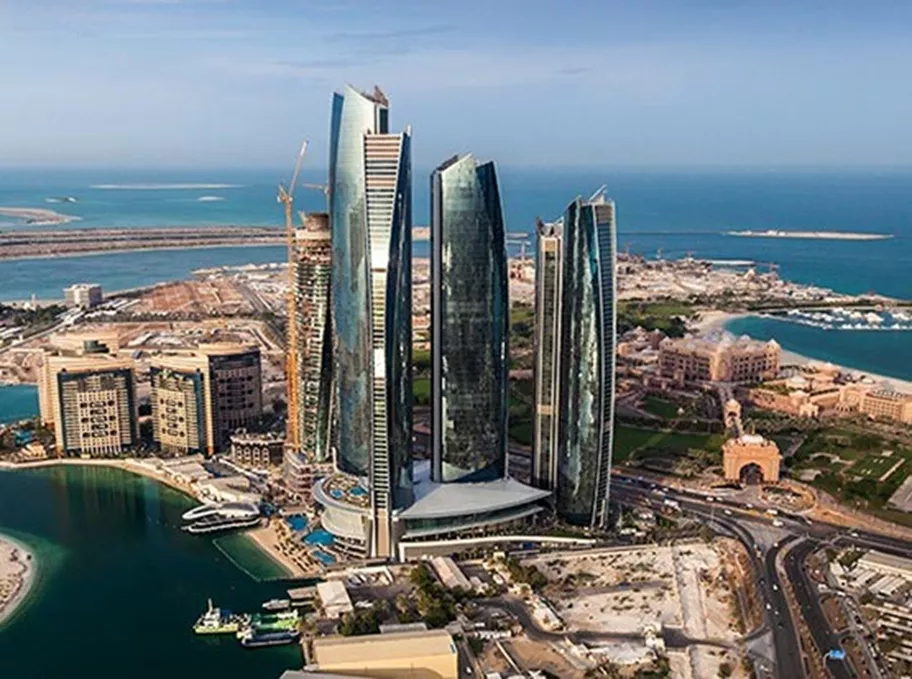 The striking Etihad Towers complex in Abu Dhabi, with its five futuristic high-rises overlooking the turquoise waters of the Arabian Gulf, surrounded by upscale developments and the nearby Emirates Palace.
